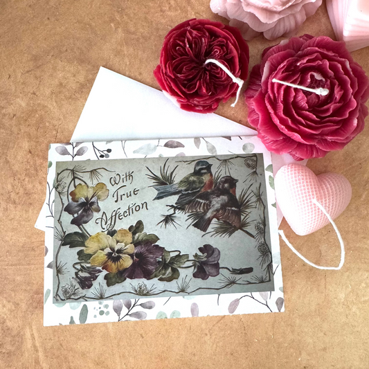 Vintage-style card with floral and bird design on a wooden surface with decorative flowers.