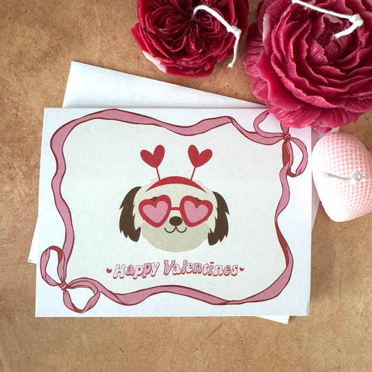 Valentine's Day card with a dog wearing heart-shaped glasses on a brown surface with flowers.